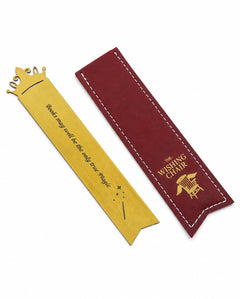 A gold-colored metal bookmark shaped like a crown with the quote 'Books may need to be the only true Magic' engraved, shown next to its dark red fabric sleeve with white stitching and gold lettering that reads 'THE WISHING CHAIR'.